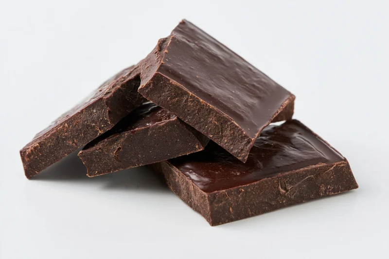 Broken dark chocolate pieces stacked loosely on white background