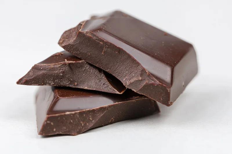 Broken dark chocolate pieces stacked loosely on white surface