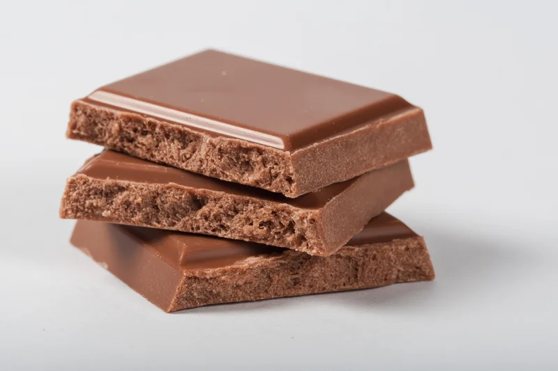 Three broken milk chocolate squares stacked loosely on a white surface