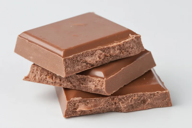 Broken milk chocolate squares stacked loosely on white background