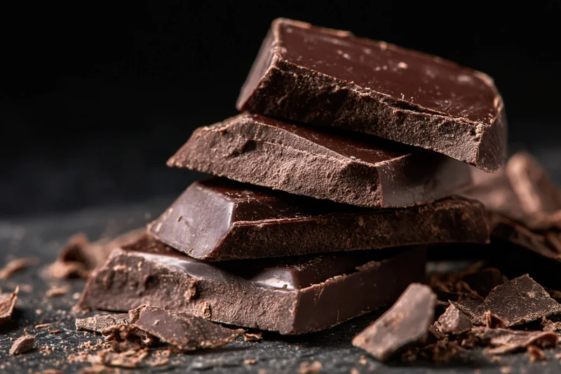 Broken dark chocolate pieces stacked unevenly on a dark surface