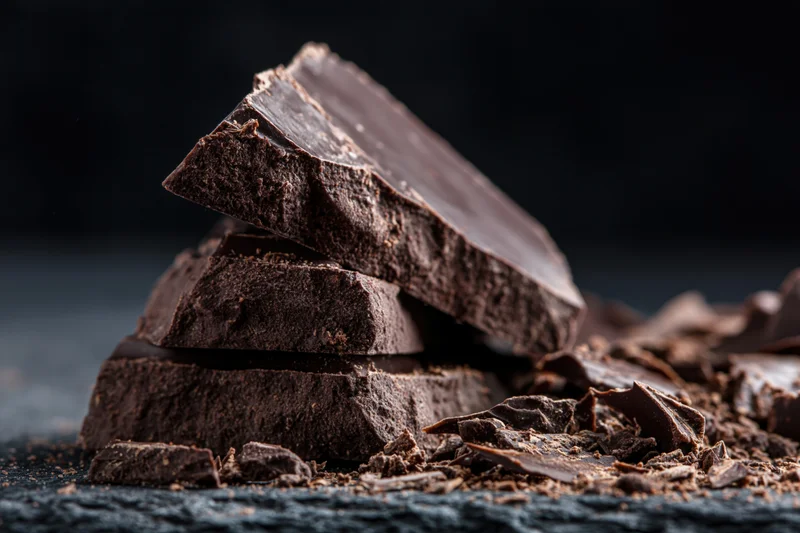 Broken dark chocolate pieces stacked unevenly on a dark stone surface