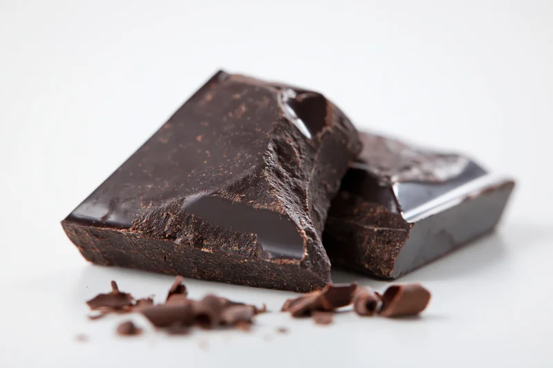 Broken dark chocolate bar pieces on white surface with crumbs scattered around