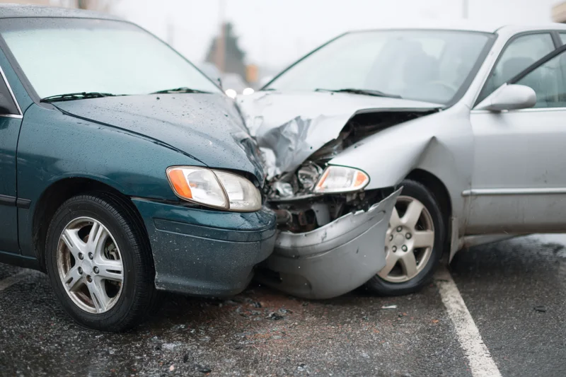 Two damaged cars with crumpled front ends pressed together in a parking lot