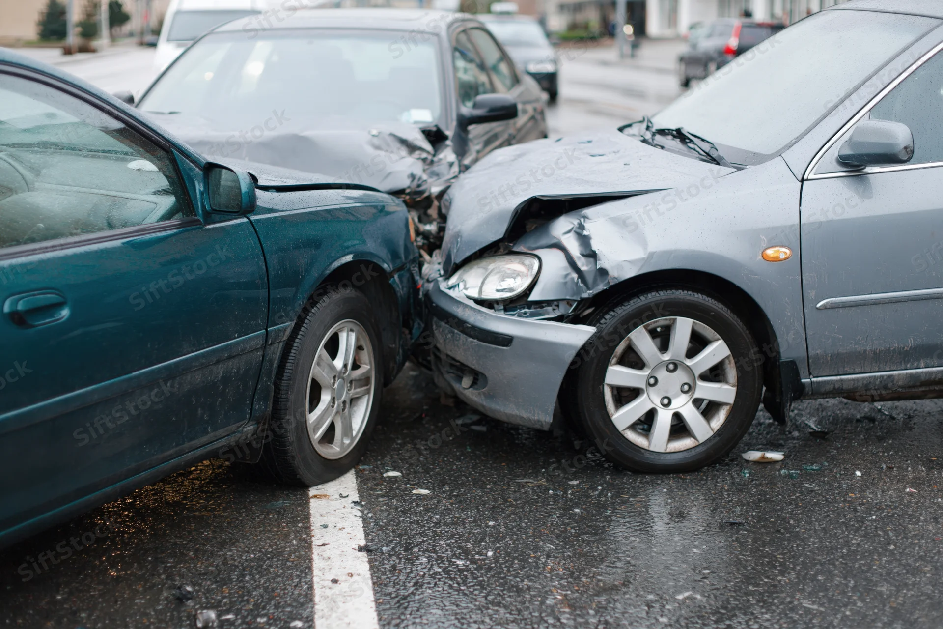 Two cars with crumpled front ends collided on a wet parking lot asphalt surface