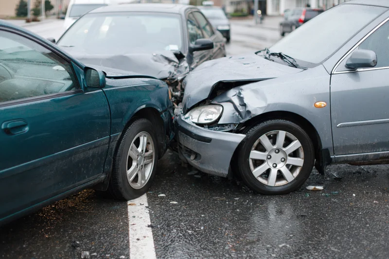 Two cars with crumpled front ends collided on a wet parking lot asphalt surface