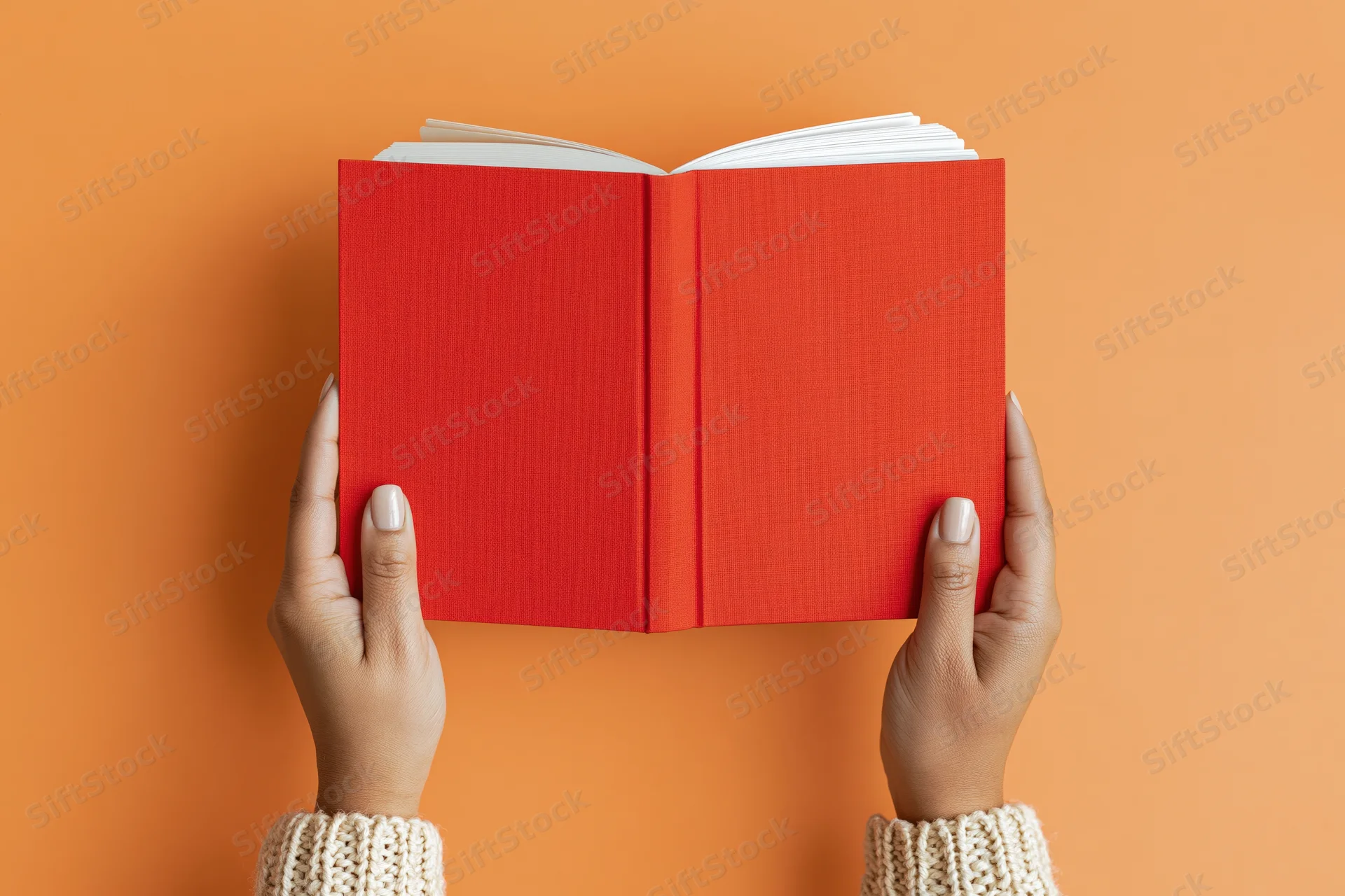 Hands holding open red hardcover book against orange background