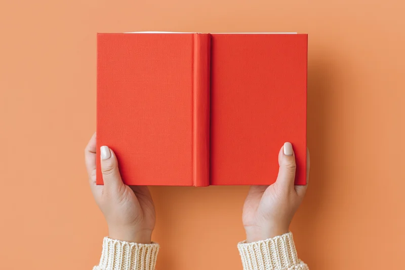 Hands holding open red hardcover book against orange background