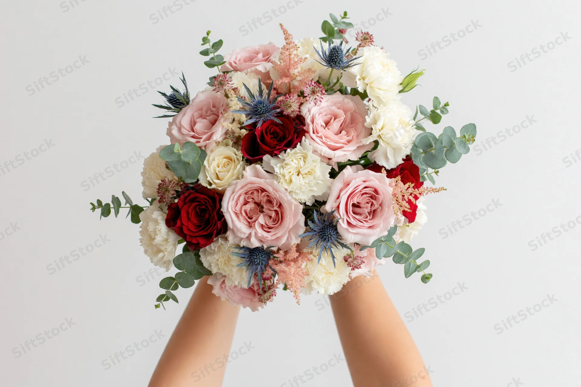 Hands holding a lush mixed flower bouquet against a plain white background