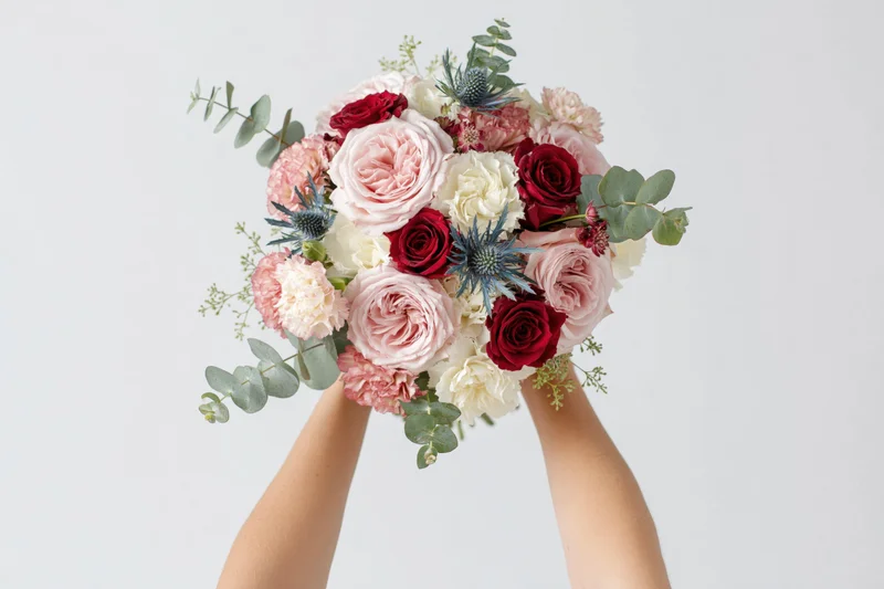Hands holding a lush mixed flower bouquet against a plain white background