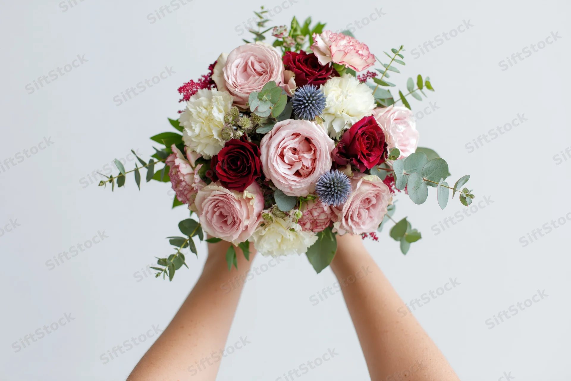 Hands holding a lush mixed flower bouquet with roses, peonies and greenery against a white background