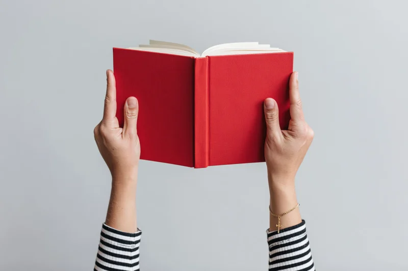 Hands holding open red hardcover book above white background