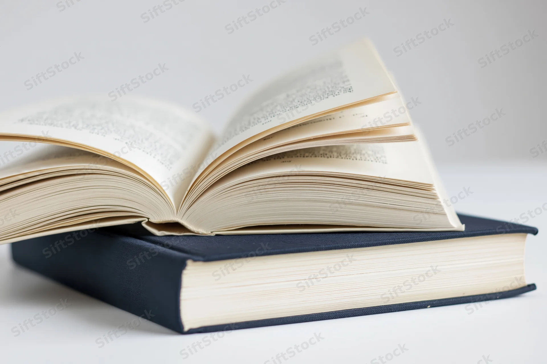 Open hardcover book resting on top of closed navy hardcover book on white surface