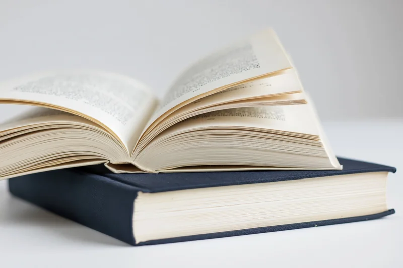 Open hardcover book resting on top of closed navy hardcover book on white surface