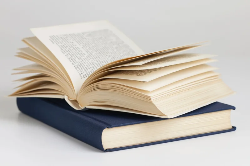 Open hardcover book resting on a closed navy blue book on a white surface