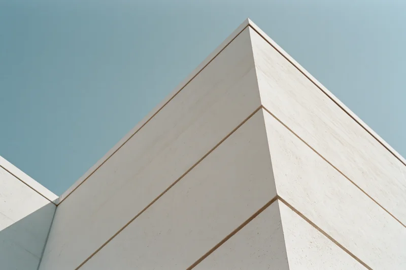 Low-angle view of a white concrete building corner with horizontal panels against a clear blue sky