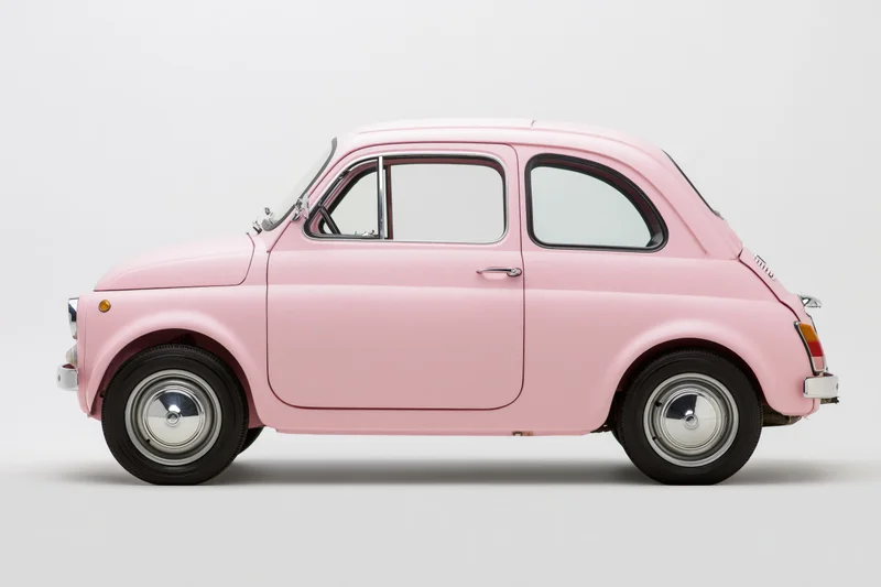 Vintage pink italian compact car shown in side profile against white background