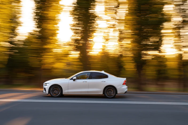White european sport sedan driving fast on asphalt road at sunset with blurred trees in background