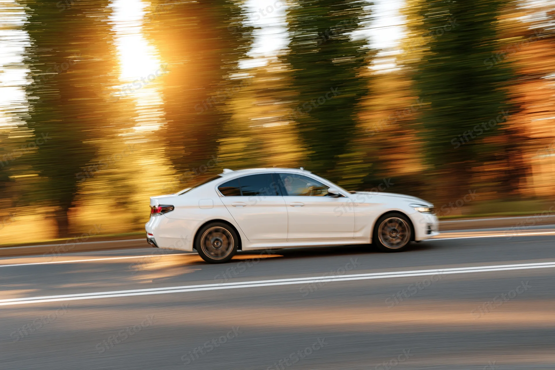 White sport sedan driving fast on asphalt road at golden hour