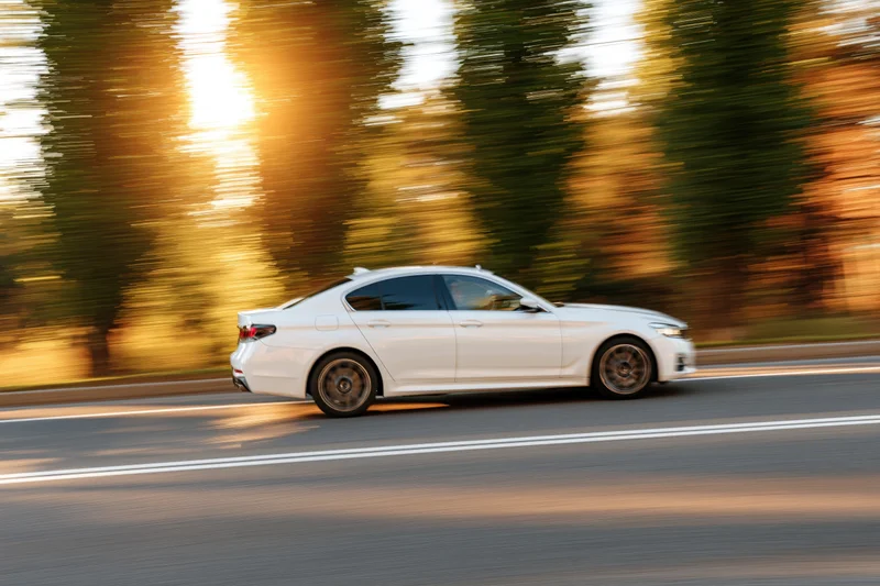 White sport sedan driving fast on asphalt road at golden hour