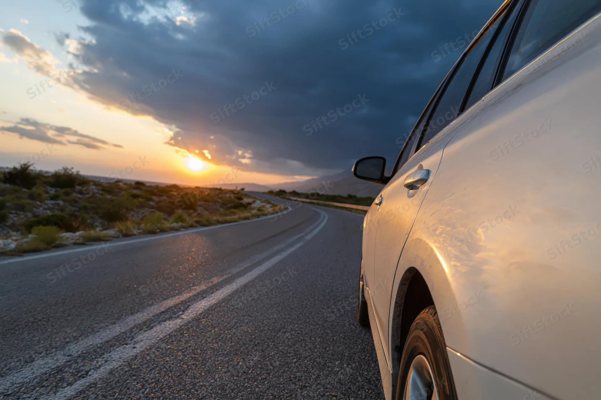 White car driving on winding highway at sunset with mountains in distance