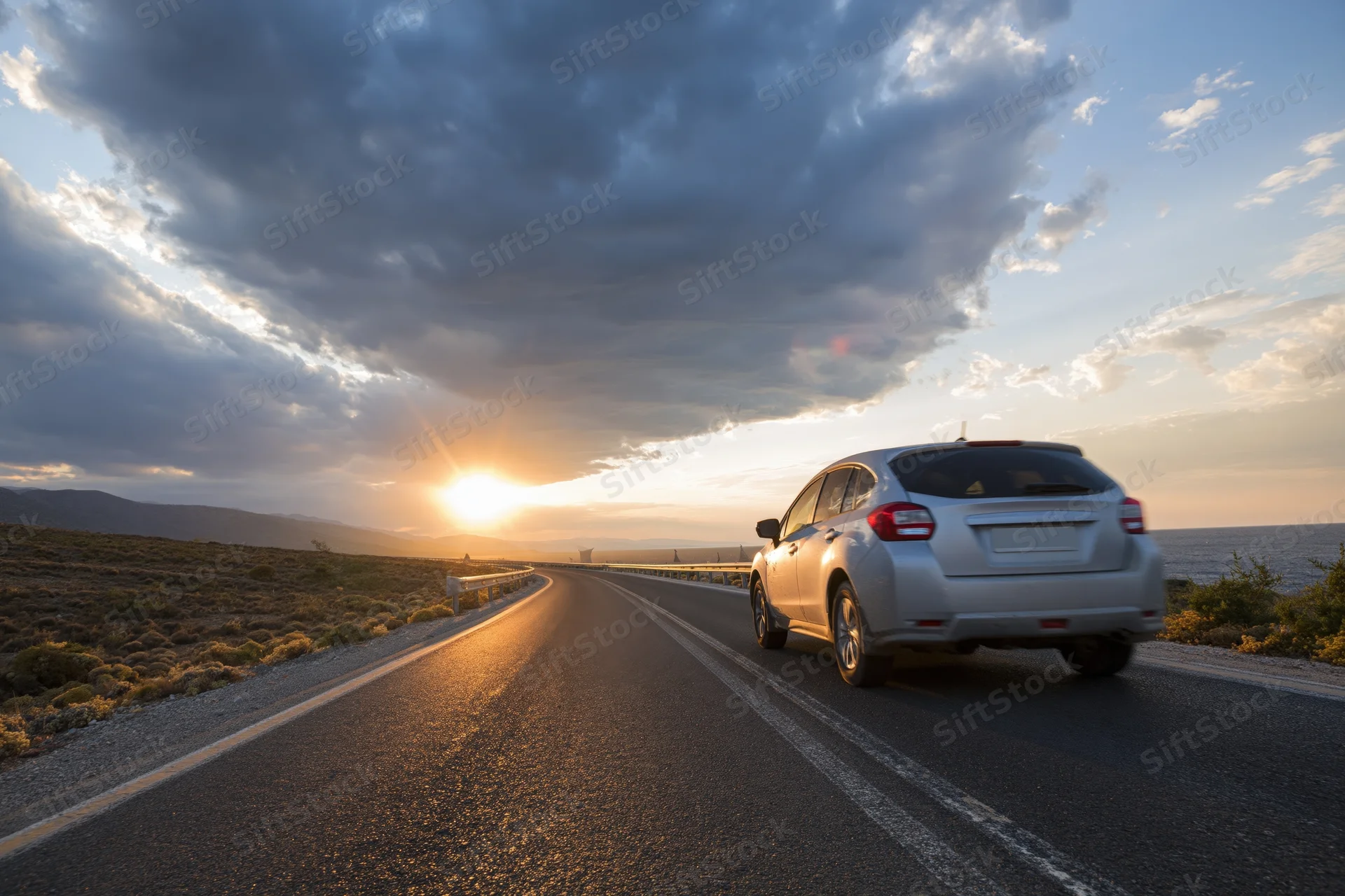 White suv driving away on a coastal highway at sunset