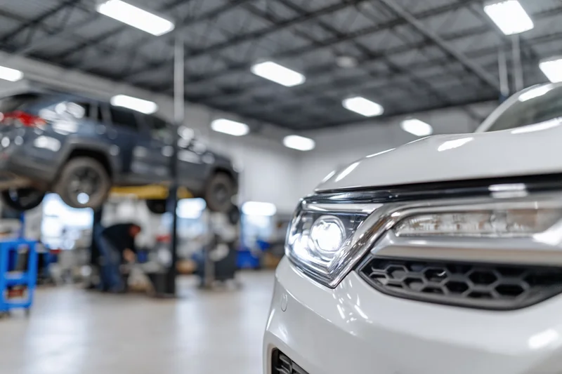 White suv front end in focus with mechanic working under lifted truck in background garage