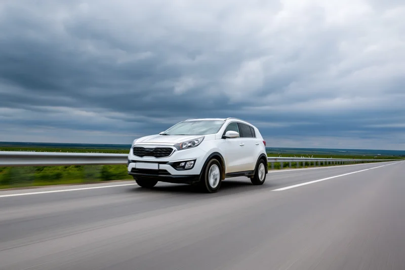 White compact suv driving on a two-lane highway under cloudy sky