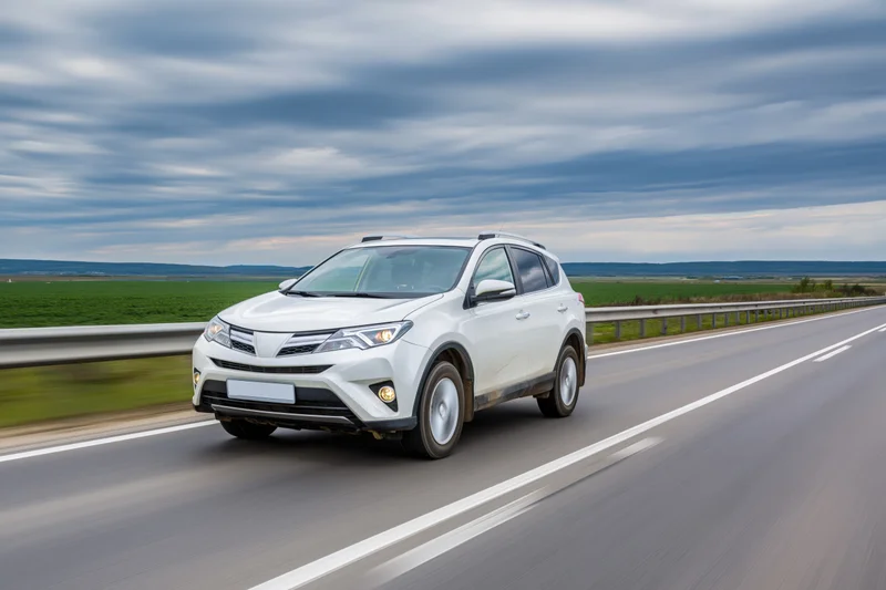 White compact suv driving on a two-lane highway with blurred motion and rural fields under cloudy sky