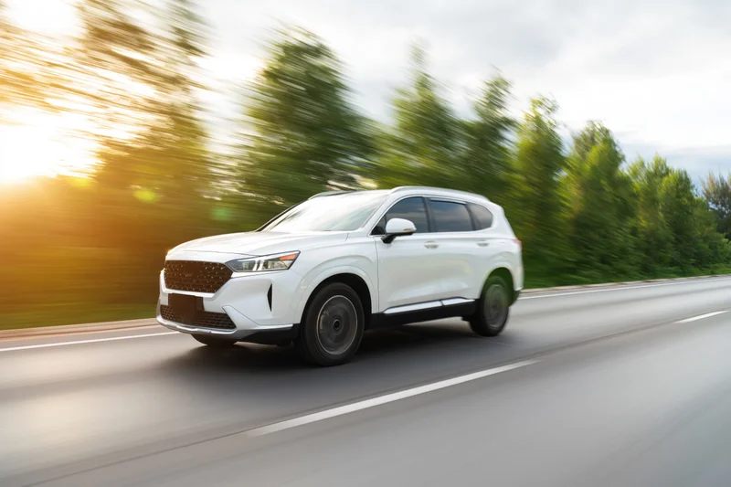 White midsize suv driving on highway with motion blur and trees in background