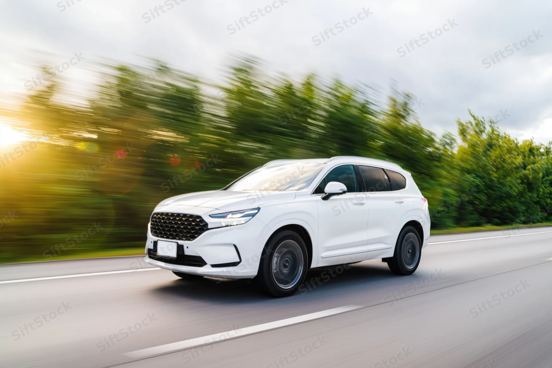White mid-size suv driving on a two-lane highway with motion blur and green trees in background