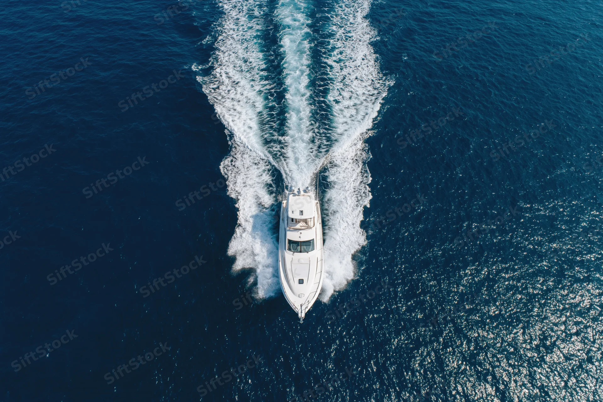 White motor yacht moving through deep blue ocean leaving a foamy wake behind