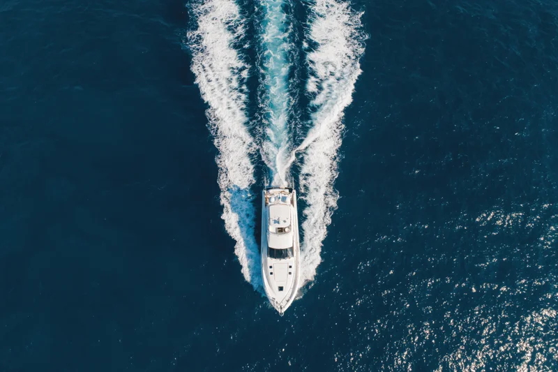 White motor yacht moving through deep blue ocean leaving a foamy wake