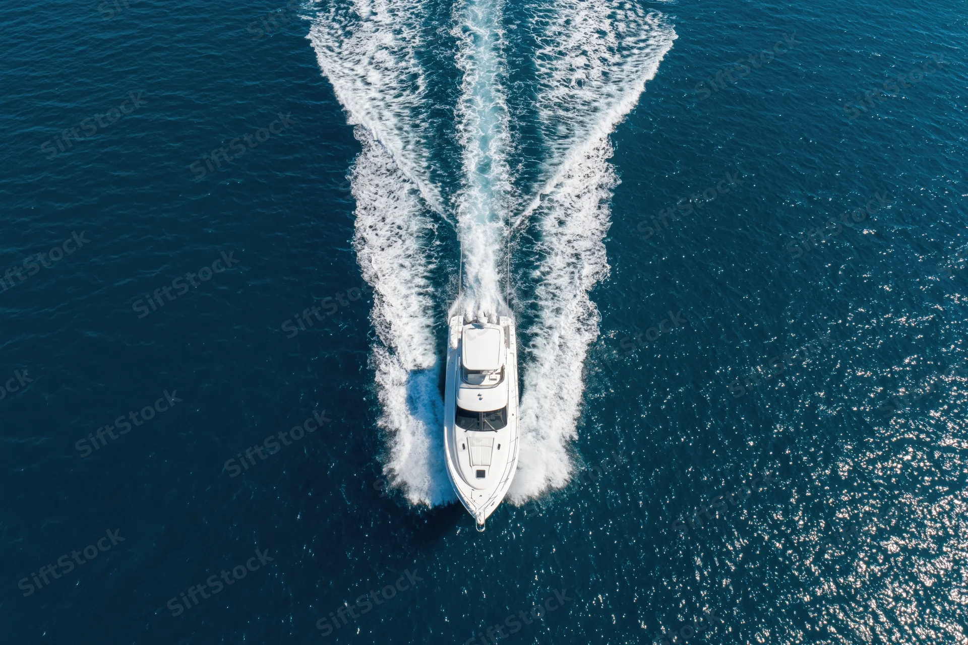 White motor yacht moving at speed across deep blue ocean leaving a foamy wake