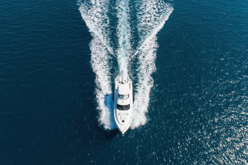 White motor yacht moving at speed across deep blue ocean leaving a foamy wake