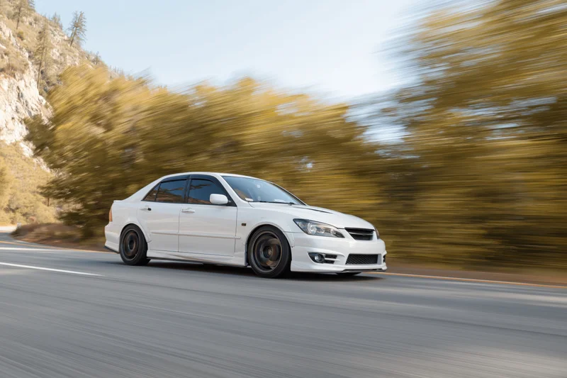 White sedan driving fast on a two-lane mountain road with motion blur