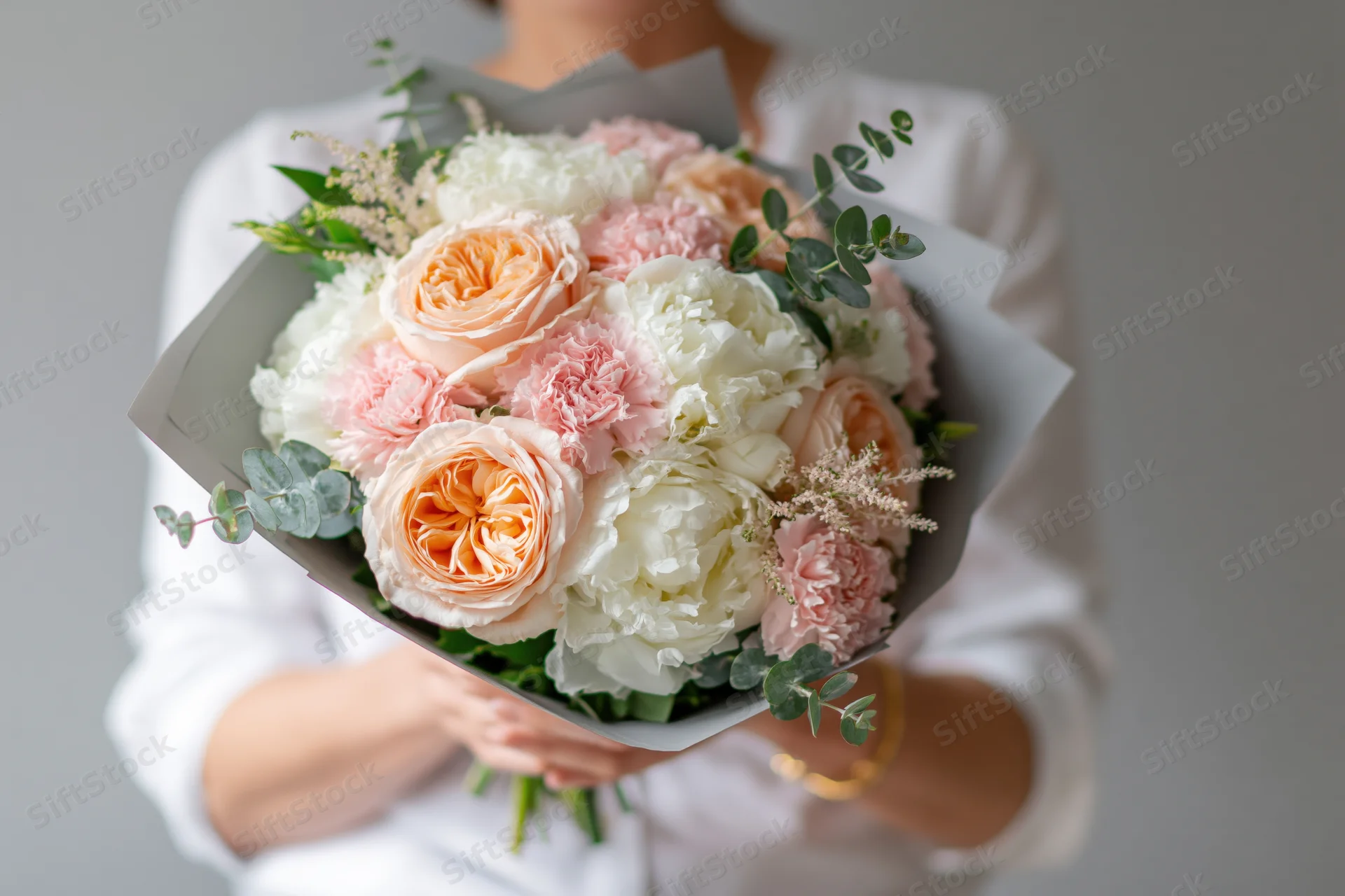 Woman holding a large wrapped bouquet of peach and white roses and peonies with eucalyptus foliage