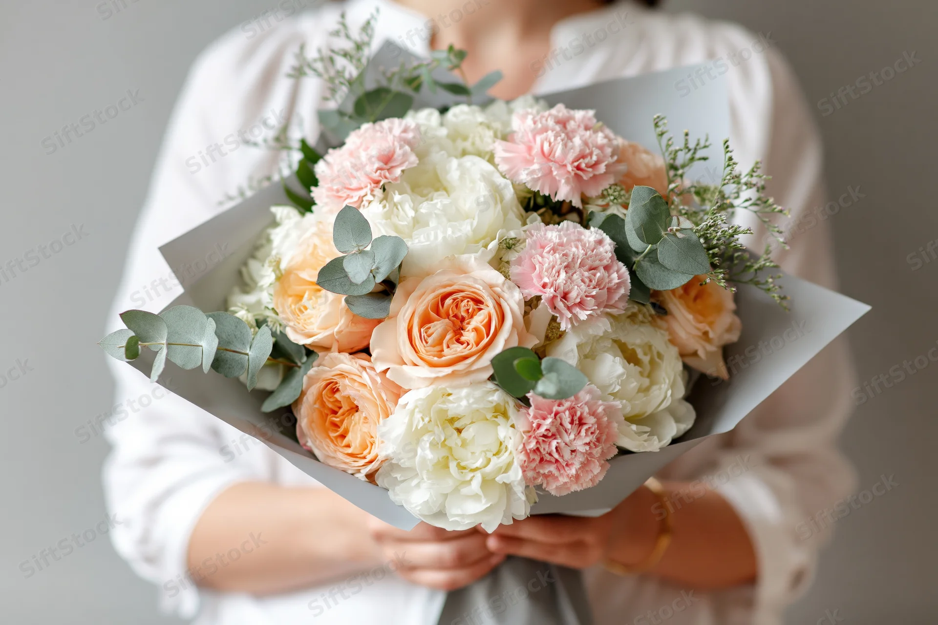 Woman holding a large wrapped bouquet of peach roses, peonies and carnations with eucalyptus greenery