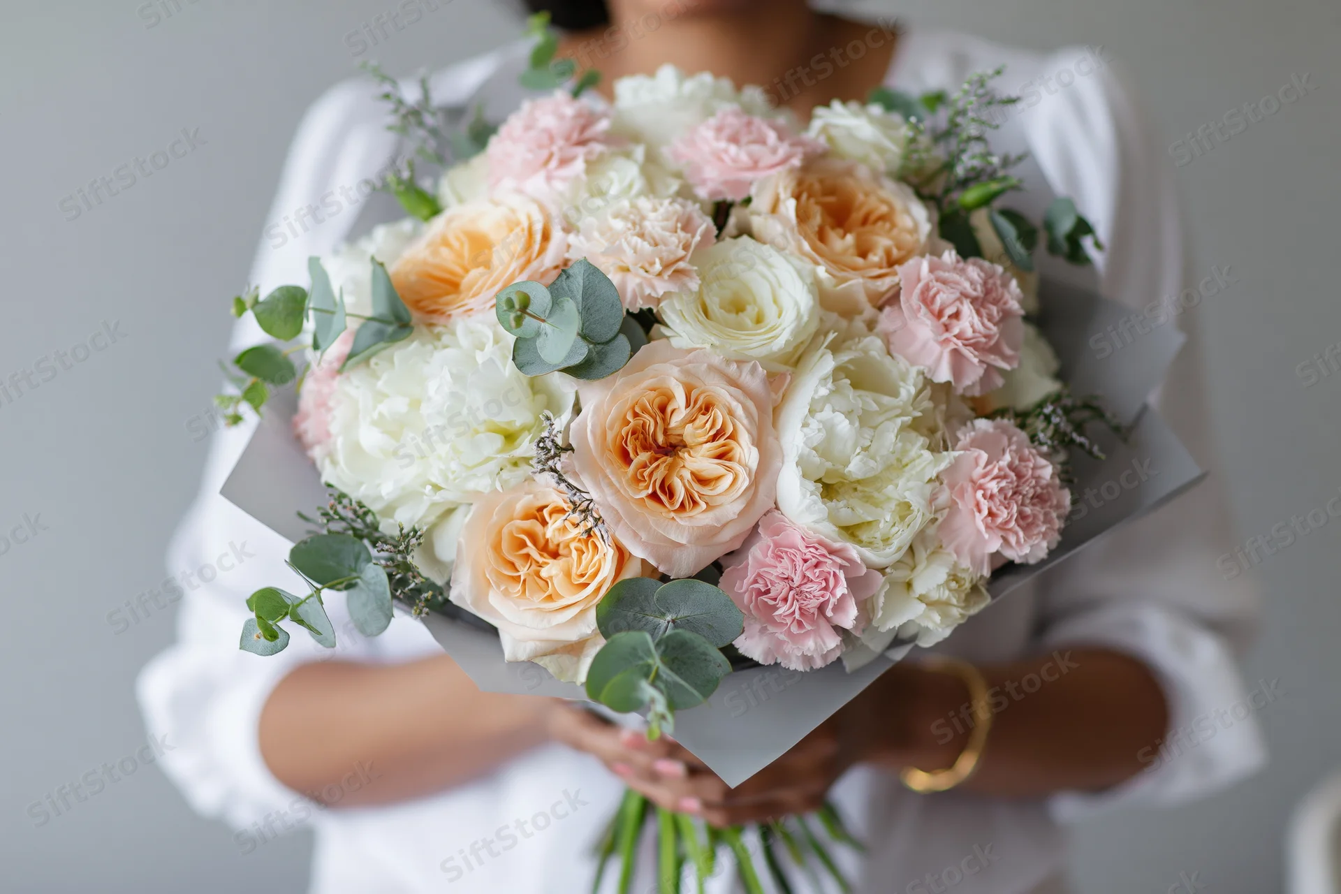 Woman holding a large wrapped bouquet of peach, pink and white flowers with eucalyptus greenery