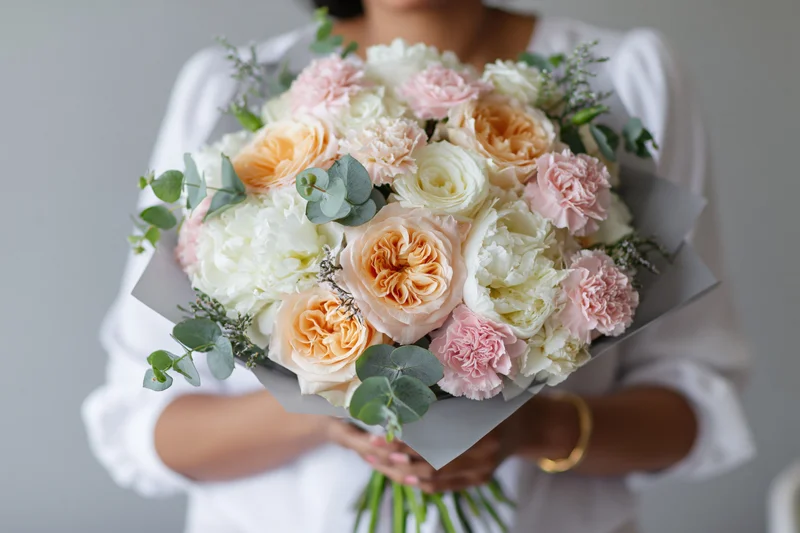 Woman holding a large wrapped bouquet of peach, pink and white flowers with eucalyptus greenery