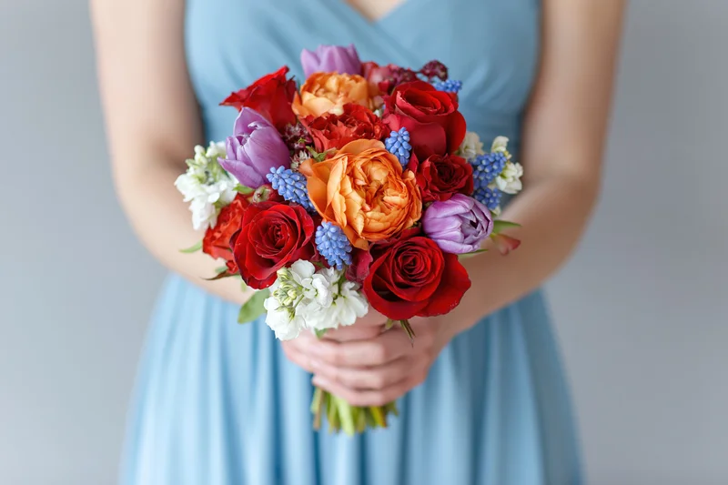 Woman holding a dense mixed flower bouquet in a light blue dress