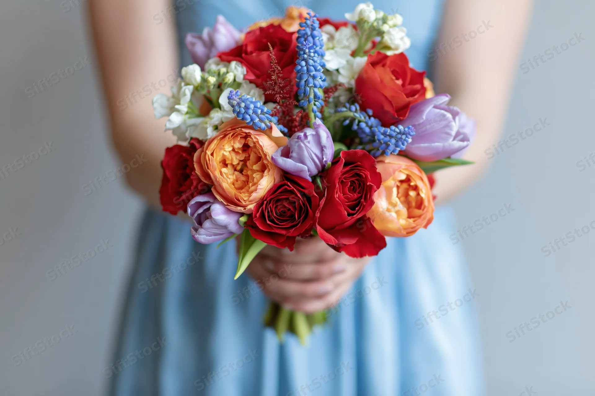 Woman holding a dense mixed flower bouquet in a light blue dress