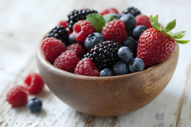 Wooden bowl filled with mixed fresh berries on a rustic table