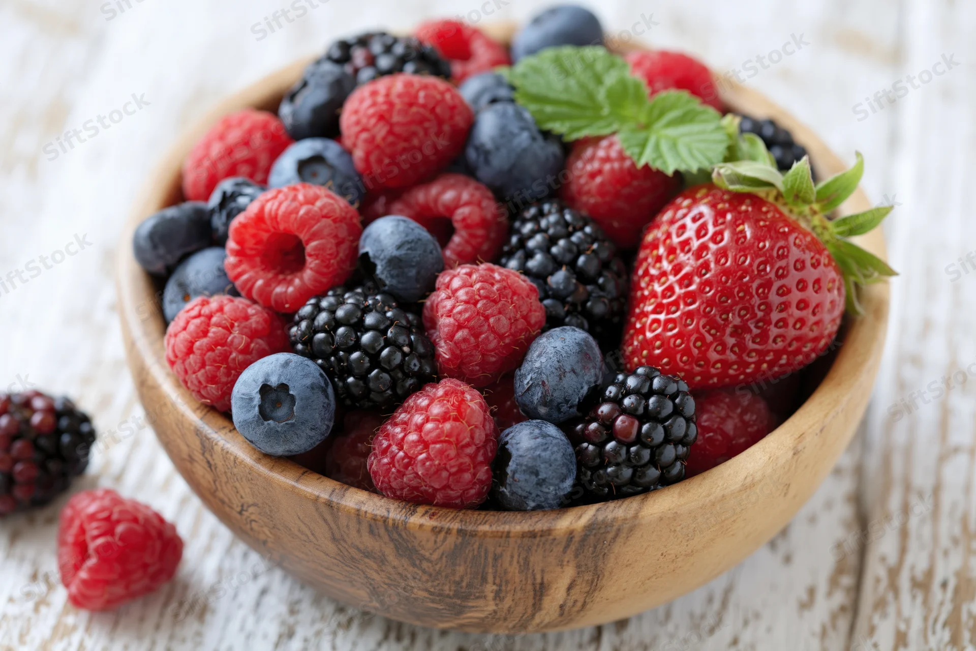 Mixed fresh berries in a wooden bowl on a white wooden surface