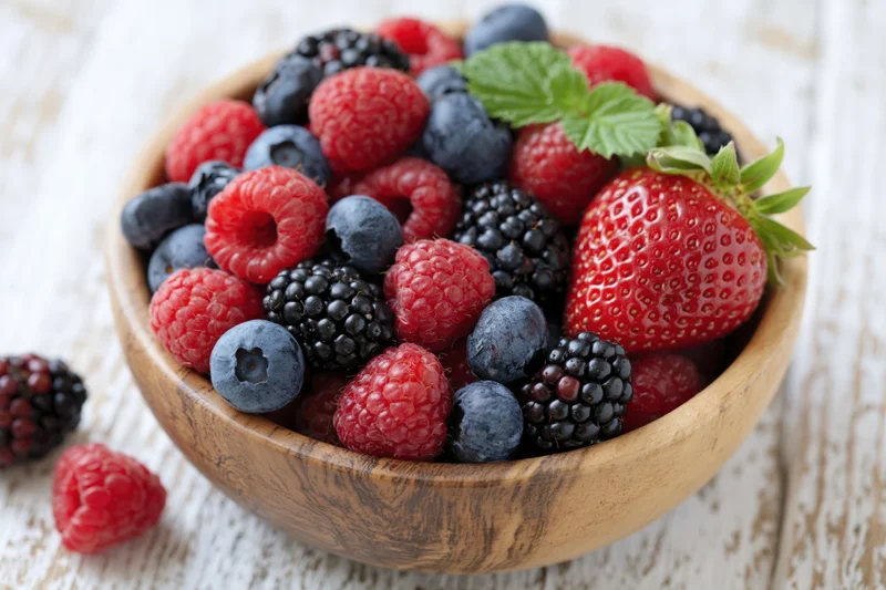 Mixed fresh berries in a wooden bowl on a white wooden surface