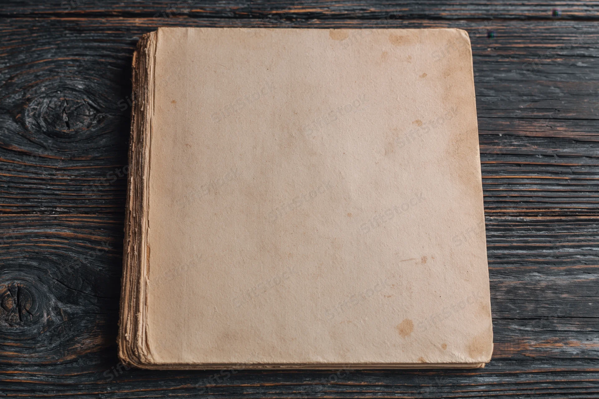 Worn antique book lying face-up on dark weathered wooden surface