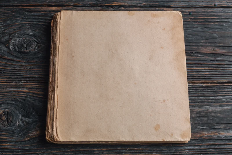 Worn antique book lying face-up on dark weathered wooden surface