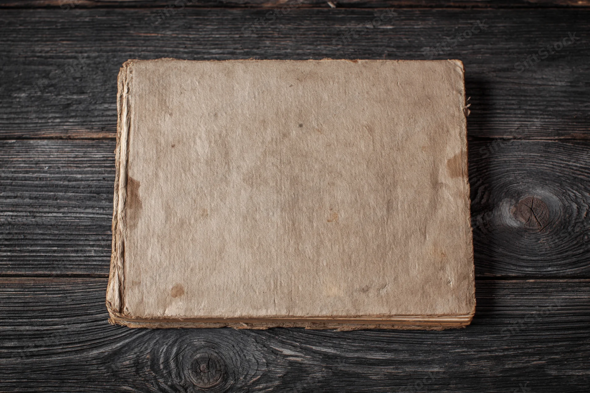 Worn antique book lying face-up on dark weathered wooden surface