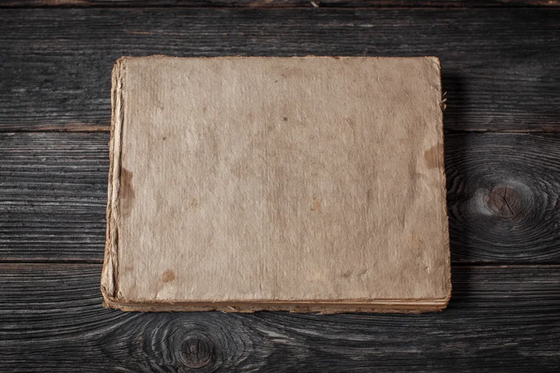 Worn antique book lying face-up on dark weathered wooden surface