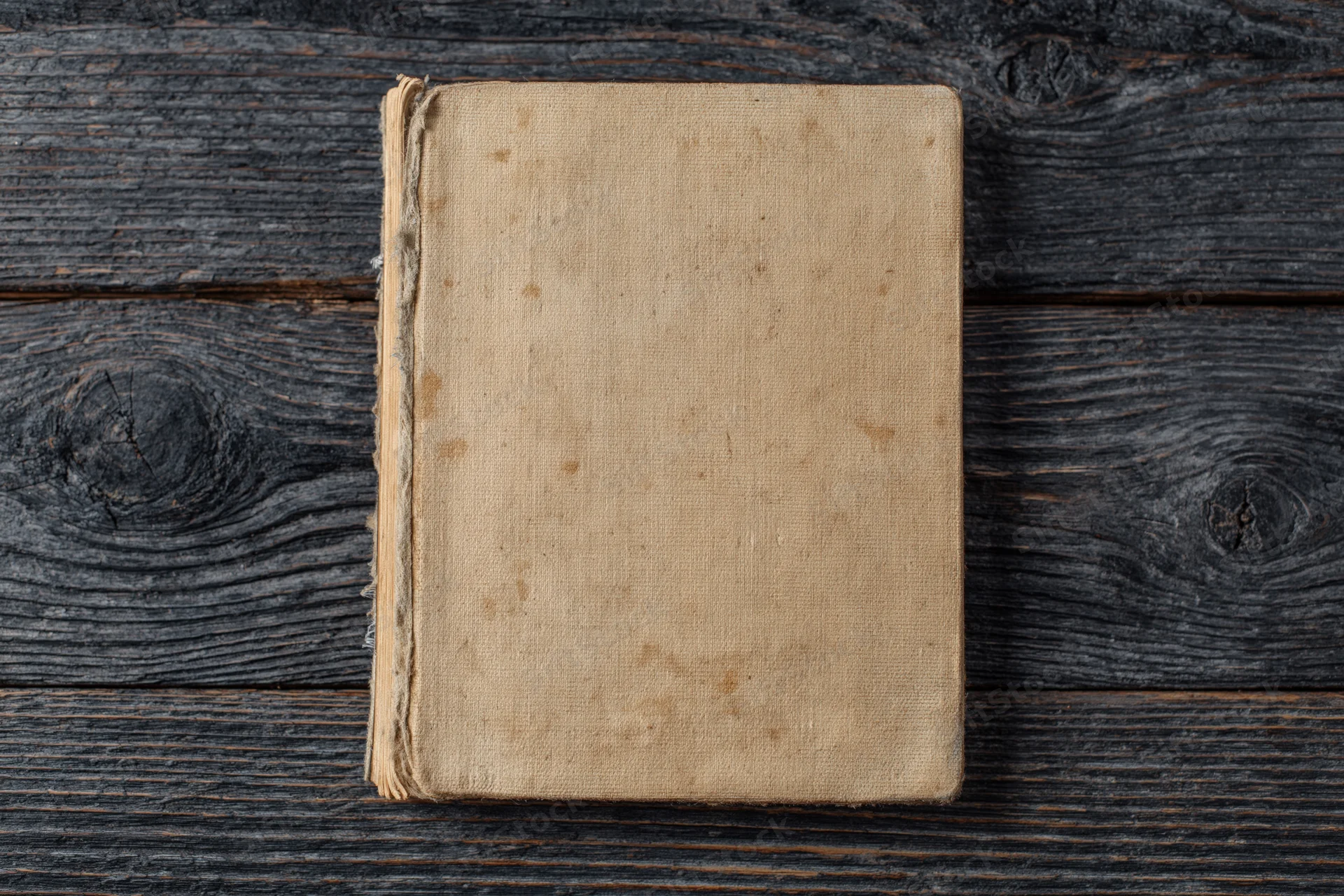 Worn antique book lying face-up on dark weathered wooden surface